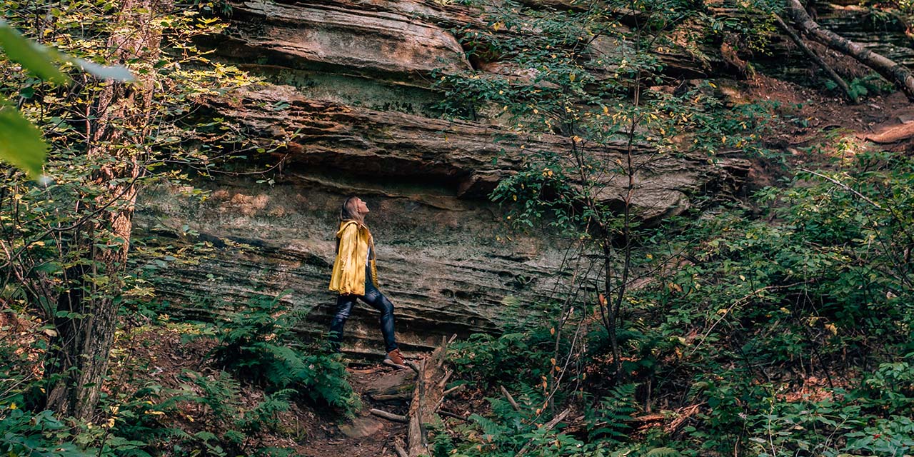 A woman walking in front off the rocky arbor state park sand stone wall