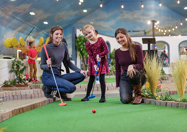 Kid and adults mini golfing indoors.