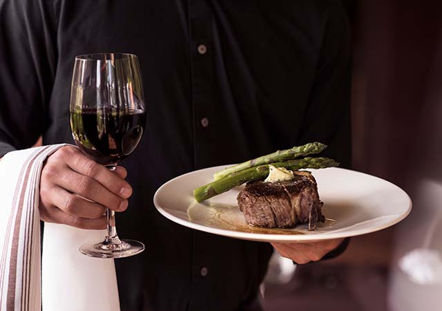 Waiter serving red wine and steak.