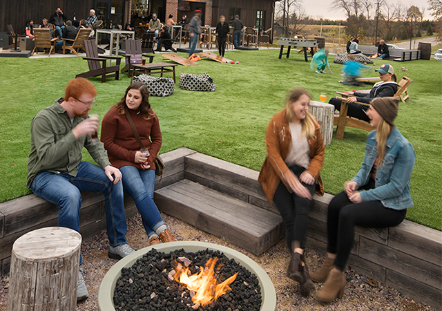 Adults sitting near a firepit and enjoying a drink