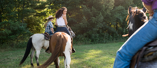 Woman smiling and riding a horse at Woodside Ranch