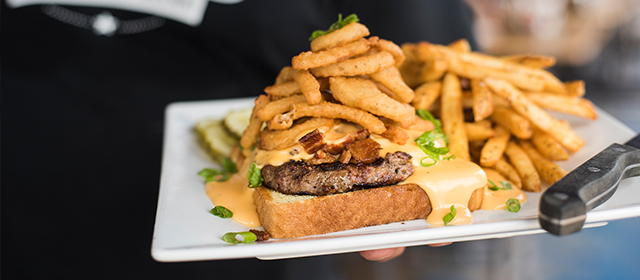 burger topped with melted cheese, fried onions on a plate with fries