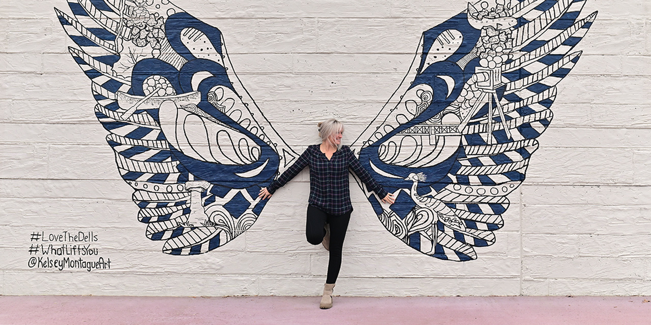 Woman posing in front of wings mural.