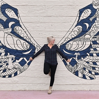 Woman posing in front of wings mural.