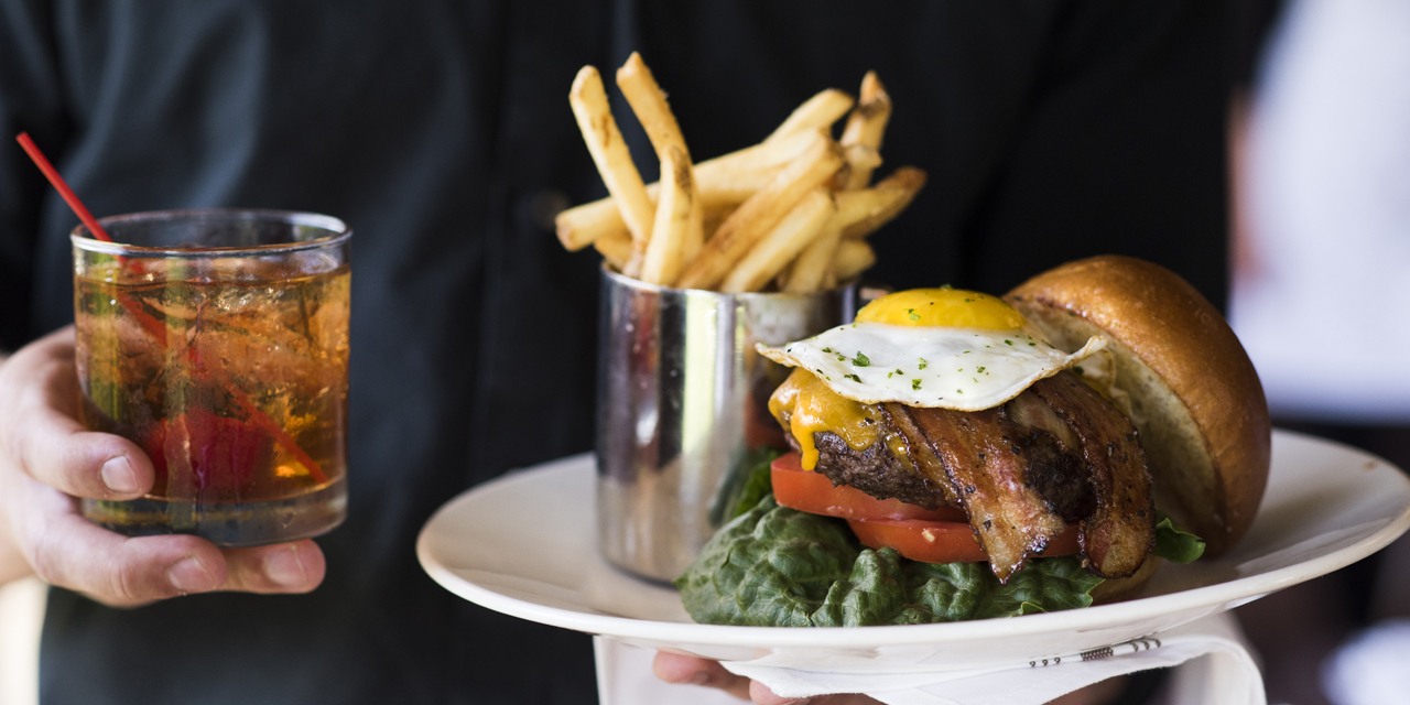 Server carrying a burger and Old Fashioned.