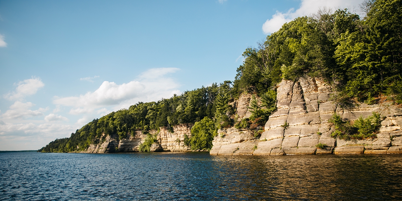 Natural rock formations and trees stand over water.