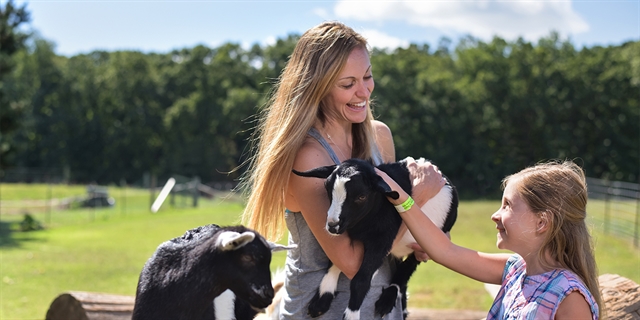 A mom and daughter pet a goat.
