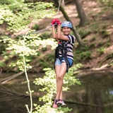 A girl zips across the forest on a zipline.