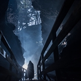 A hooded figure stands silhouetted in a spooky gulch.