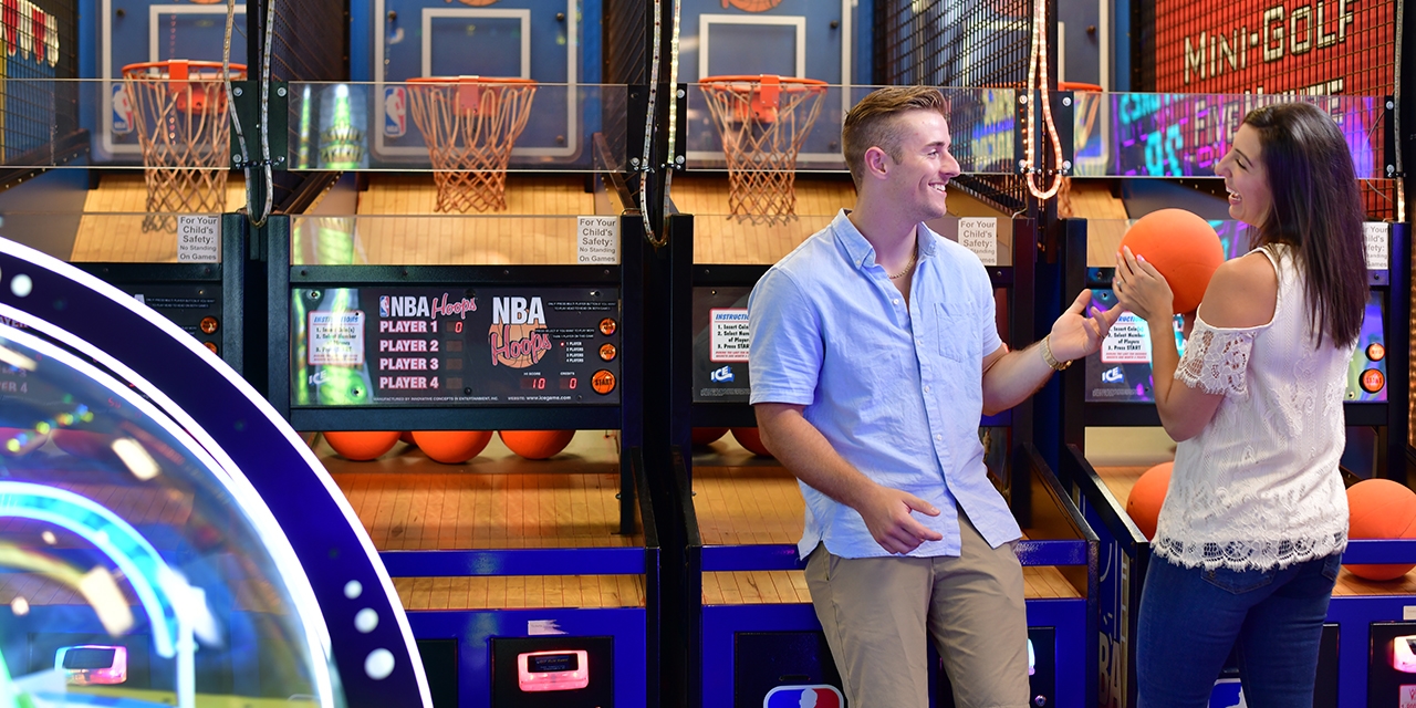 A couple plays a basketball arcade game.