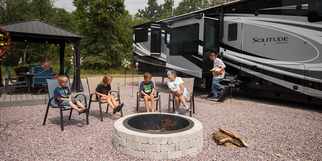 A family sits around a fire pit at a campsite.
