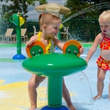 Children play in the splash area with tables and chairs in the distance.
