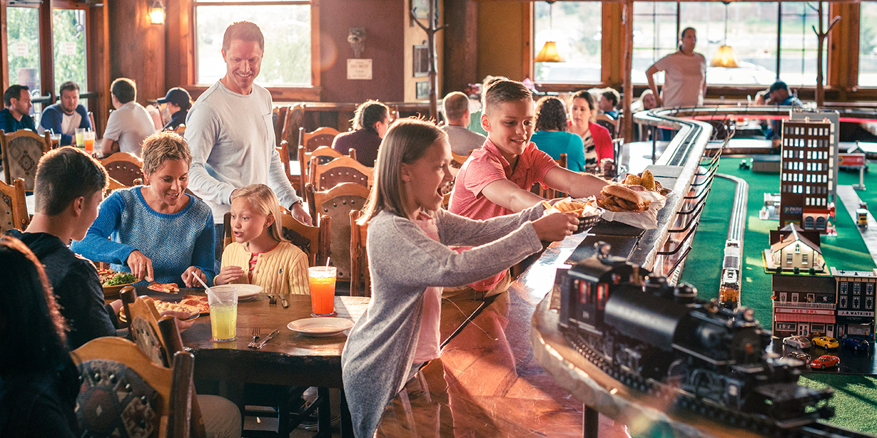 Families dining at Buffalo Phil's Pizza & Grille with children receiving their food from a model tra