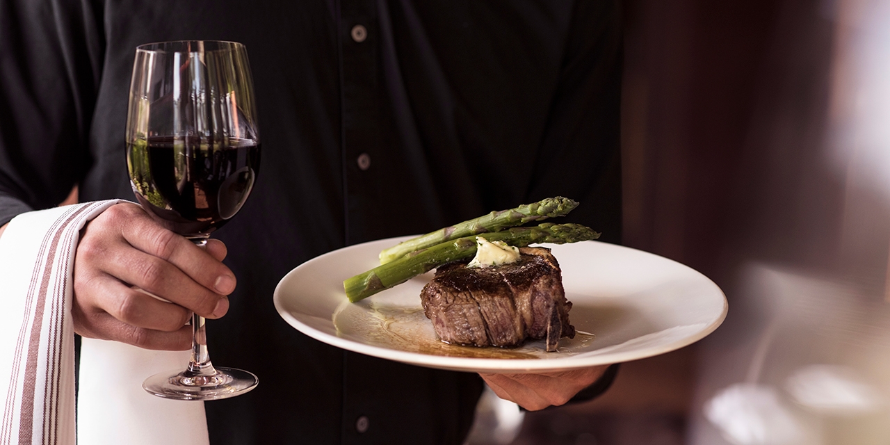 A server with a steak and asparagus and a glass of wine.
