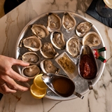 A woman grabs and oyster from a large plate of oysters.