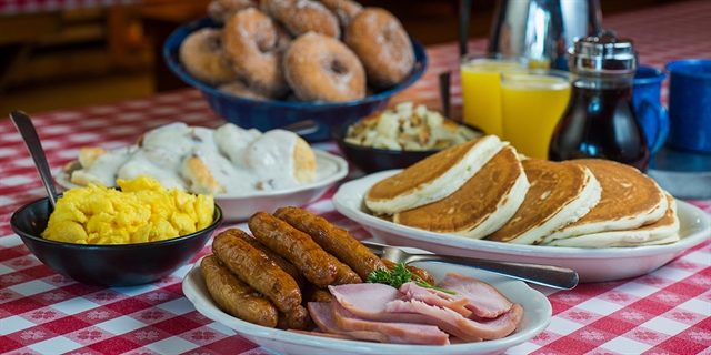 A selection of breakfast items including pancakes, breakfast sausage, scrambled eggs, and doughnuts.
