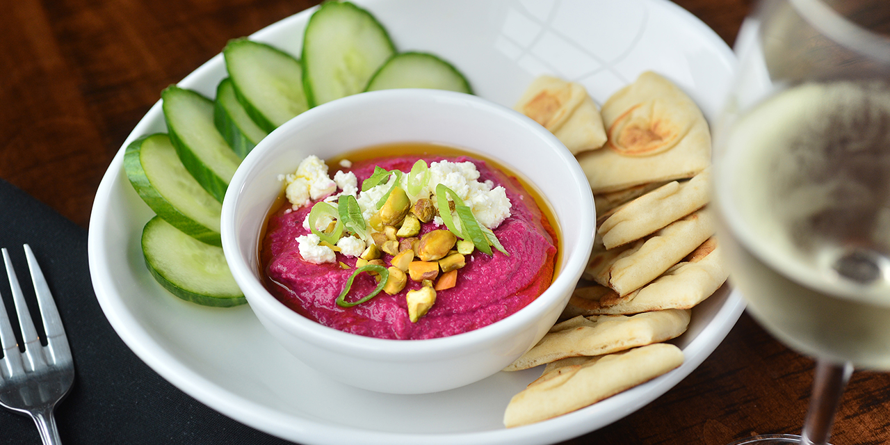 A roasted beet hummus bowl with pita and cucumbers.