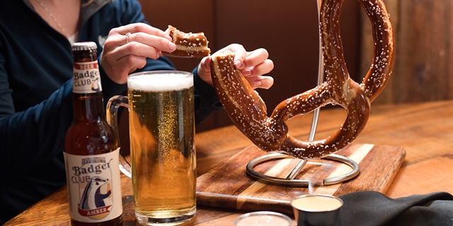 A woman enjoying a pretzel and beer.