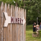 A sign pointing toward the winery with people enjoying their time together in the background.